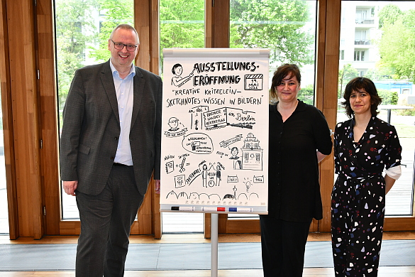 Zu sehen ist der Bevollmächtigte Dr. Olaf Joachim, Maria Santos und Dr. Maria Nunes Haus der Wissenschaft, neben der gezeichneten Sketchnote der Veranstaltung.